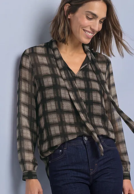 Vrouw in transparant ruitblouse met strik en hoge taille jeans, glimlachend voor een effen achtergrond