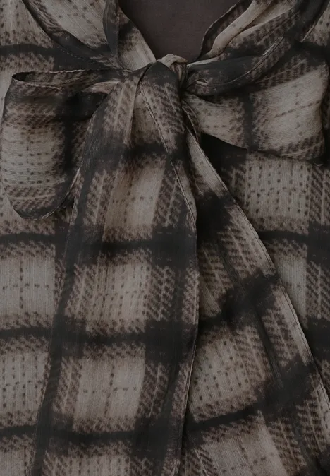 Close-up van een crème-zwart geruit stof die in een strik bij de halslijn is gebonden.