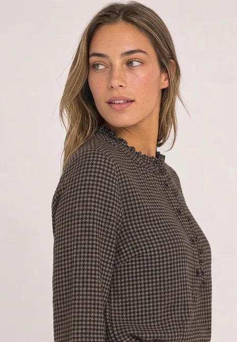 Jeune femme en chemisier à carreaux et volants, regard de côté, style élégant et décontracté.