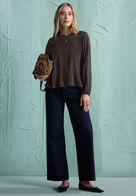 Chemisier à manches longues et à basque black coffee Eine Frau in braunem Langarmshirt, weitem dunkelblauen Hosen und schwarzen Pumps, trägt eine braune Tasche.