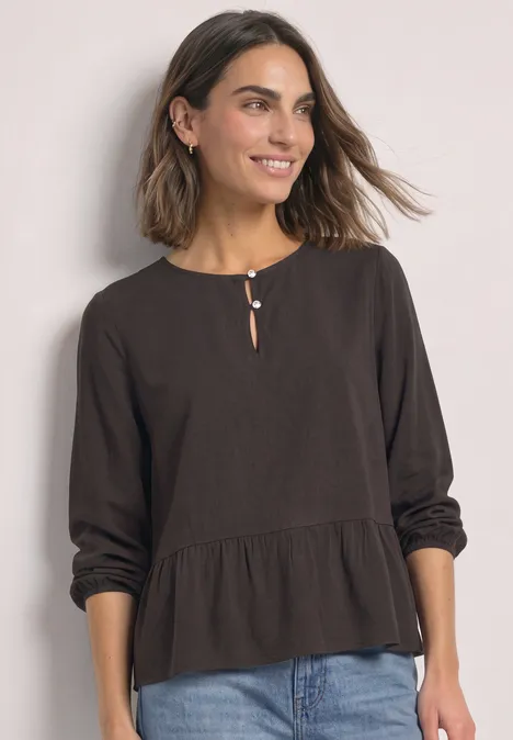 Chemisier à manches longues et à basque black coffee Frau trägt schwarze, lockere Bluse mit langen Ärmeln, Knopfdetail am Ausschnitt und lockerer Passform zu Jeans.