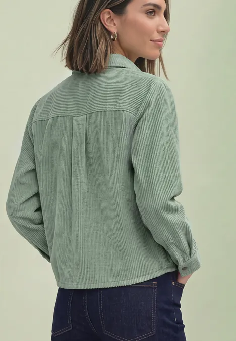 Frau mit grüner Cordjacke und Jeans, von hinten vor einfarbigem Hintergrund.