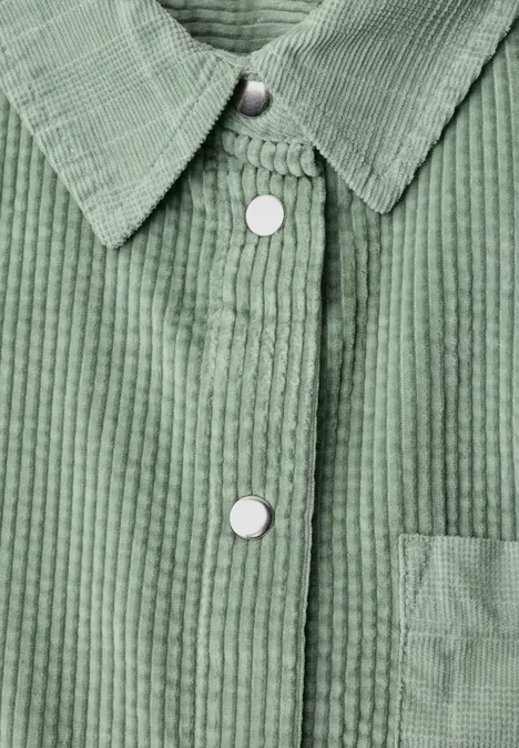 Grüne Cordjacke mit weißen Druckknöpfen und aufgesetzter Tasche.