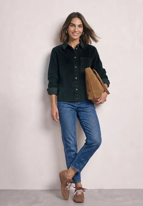 Vrouw in zwart corduroy-overhemd, blauwe jeans, bruine laarsjes, met een cognackleurige tas.