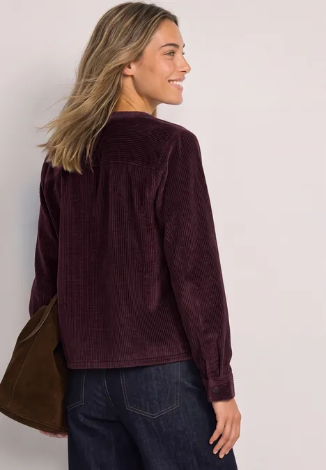 Frau von hinten mit violetter Cordjacke, blonden Haaren und Jeans, trägt eine Tasche über der Schulter.