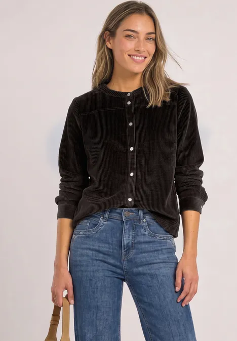 Junge Frau in schwarzem Samtblazer und blauer Jeans, lächelt und hält eine Tasche.
