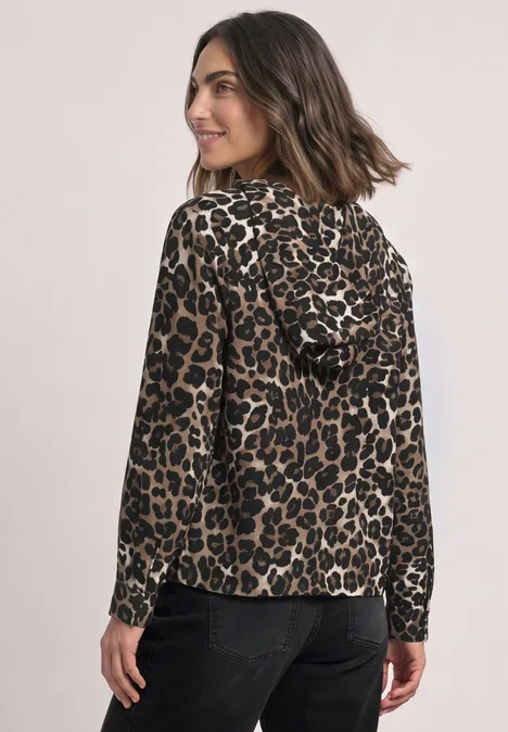 Bluse mit Kapuze und Leo-Muster Black Frau im Leoparden-Kapuzenshirt, langärmelig, blickt über die Schulter, kombiniert mit schwarzer Hose.