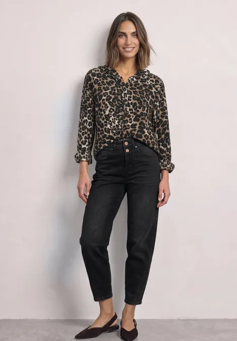 Bluse mit Kapuze und Leo-Muster Black Frau in Leo-Bluse und schwarzen Jeans steht vor neutralem Hintergrund und lächelt entspannt.