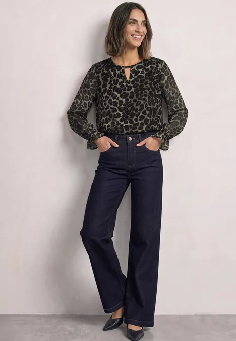 Tunika aus Chiffon mit Cut-Out-Detail Black Frau in Leopardenbluse und dunkler Schlagjeans, lächelnd mit Händen in den Taschen.