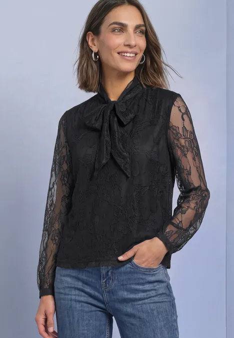 Frau trägt schwarze Spitzenbluse mit Schleife und blauen Jeans.
