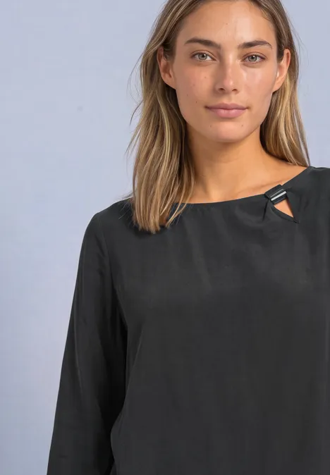 Blouse col rond à boucle décorative armor grey Une femme aux cheveux châtains longs portant un chemisier noir à manches longues sur fond neutre.