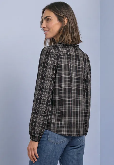 Eine Frau trägt eine karierte Bluse und Jeans und blickt seitlich über die Schulter.
