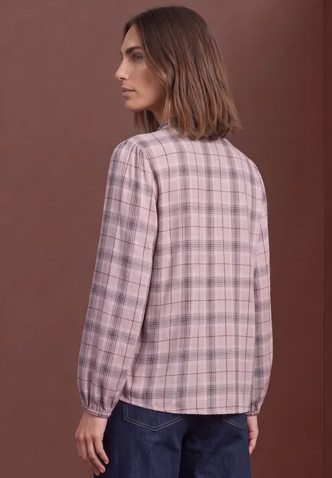 Frau von hinten in rosa kariertem Langarmhemd und Jeans vor braunem Hintergrund.