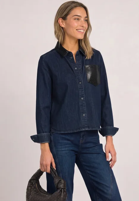Vrouw draagt donkerblauwe spijkerjas en jeans, houdt een zwarte tas vast.