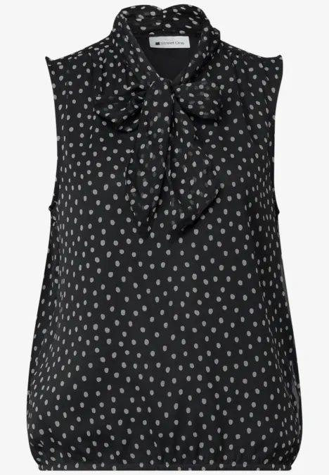 Ärmellose schwarze Bluse mit weißen Punkten und gebundenem Schleifenkragen.