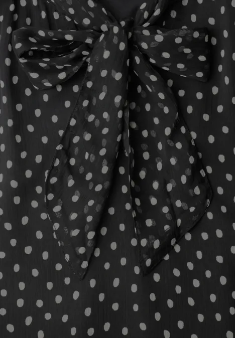 Schwarze Bluse mit weißen Polka-Dots und Schleifenbinder am Ausschnitt.