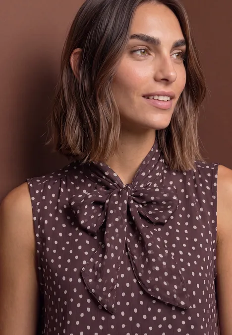 Haut-blouse en chiffon avec nœud décoratif berry plum Femme en blouse marron sans manches à motif de coeurs blancs et nœud au col, fond brun.