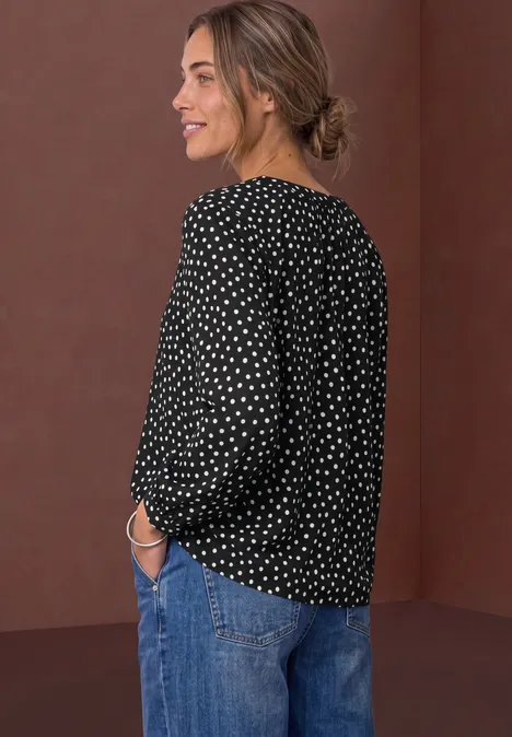 Chemisier à manches longues, à col fendu et imprimé Black Frau im Profil trägt schwarze gepunktete Bluse und Jeans, lächelnd.