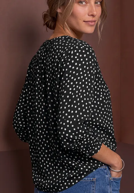 Chemisier à manches longues, à col fendu et imprimé Black Frau im schwarzen Polka-Dot-Shirt und blauen Jeans, blickt über die Schulter.