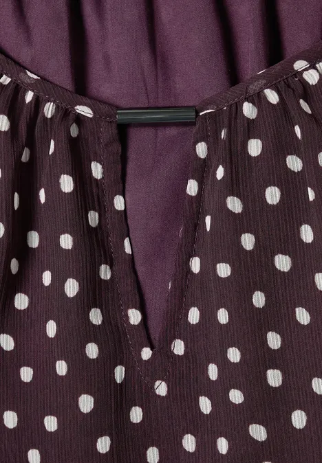 Violette Bluse mit weißen Polka Dots und V-förmigem Ausschnitt.