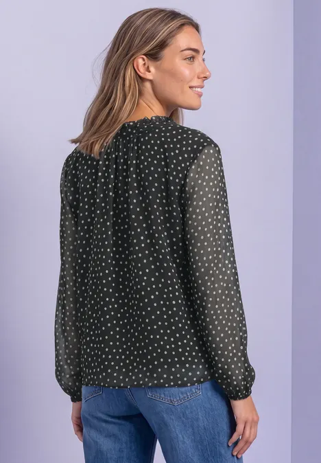 Frau in schwarzer, gepunkteter Chiffonbluse und blauen Jeans vor zweifarbigem lila Hintergrund.