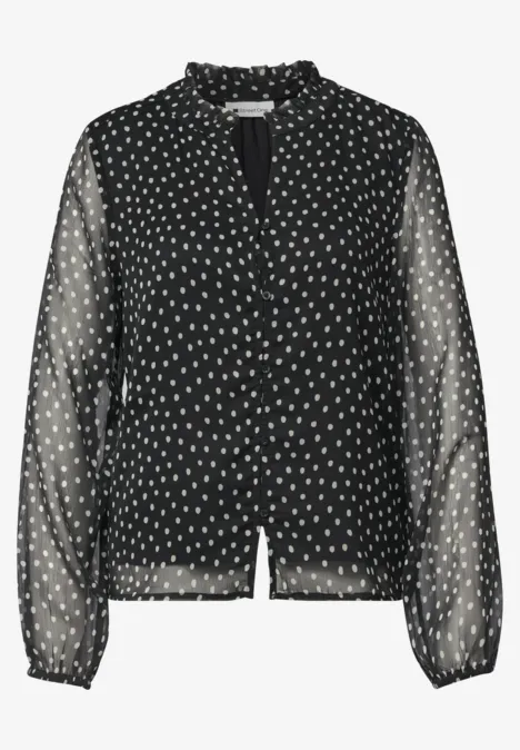 Schwarze, semitransparente Bluse mit weißen Tupfen, Rüschenkragen und langen Ärmeln.