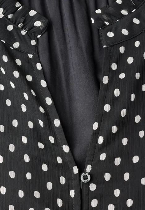 Schwarzer Stoff mit weißen Polka-Dots, mittig teilbar mit Knopf, gekräuselter Kragen.