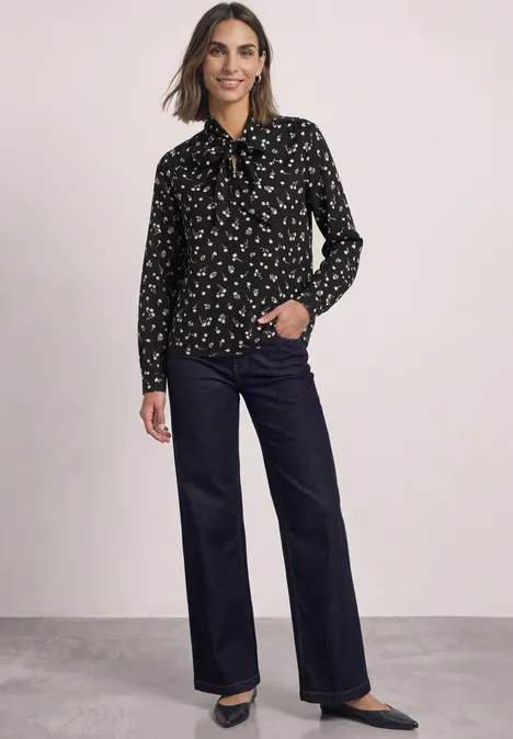 Model in schwarzer Bluse mit feinem Muster und weiter, dunkelblauer Hose, kombiniert mit schwarzen Pumps.