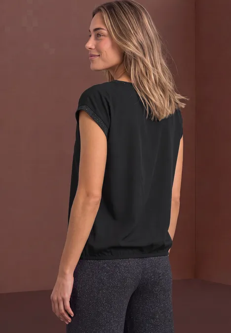 Damen-Sportoutfit: schwarzes T-Shirt, graue Leggings, seitlicher Blick auf braunem Hintergrund.