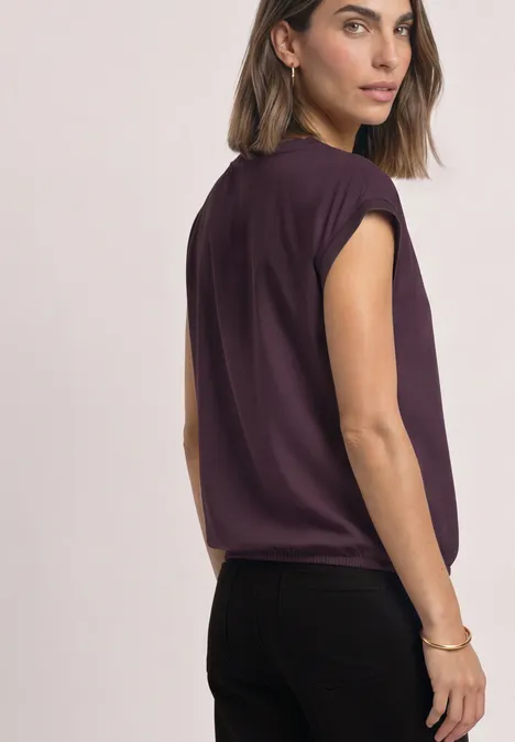 Blouse courtes manches à col rond et bandes pailletés berry plum Une femme porte un top sans manches violet et un pantalon noir, regarde par-dessus l'épaule.
