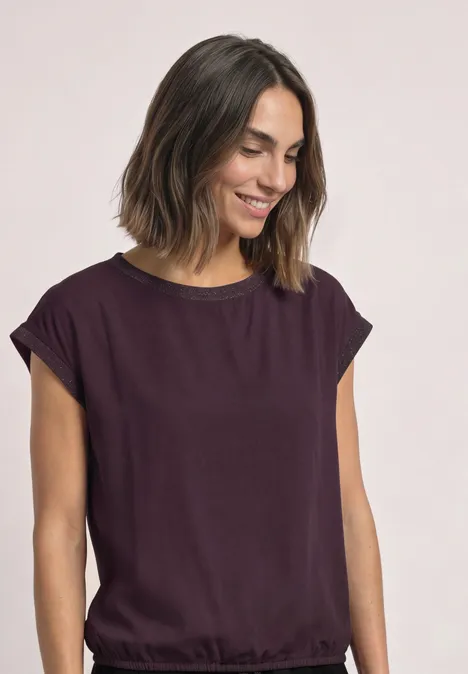 Blouse courtes manches à col rond et bandes pailletés berry plum Femme dans un top violet ample, sourit en regardant vers le bas, fond neutre.