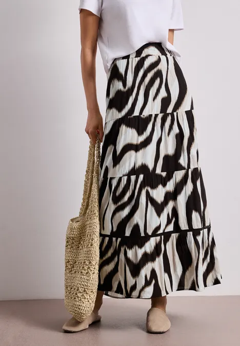 Weißes Top, langer Rock mit schwarz-weißem Zebramuster, Basttasche und flache Schuhe.