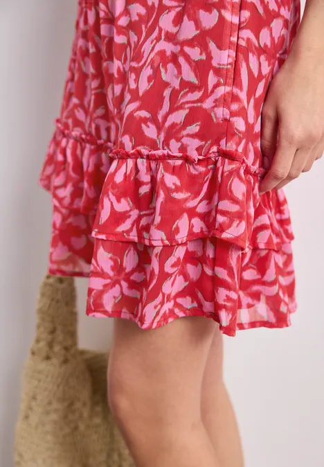 Roter Stufenrock mit rosa Blattmuster und Rüschen, Knielänge, daneben eine Basttasche.