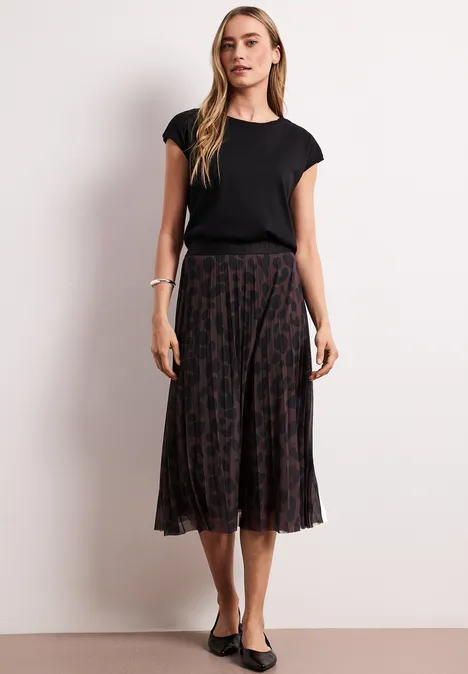 Vrouw in zwarte T-shirt en geplisseerde midirok met subtiel patroon, gecombineerd met ballerina’s.