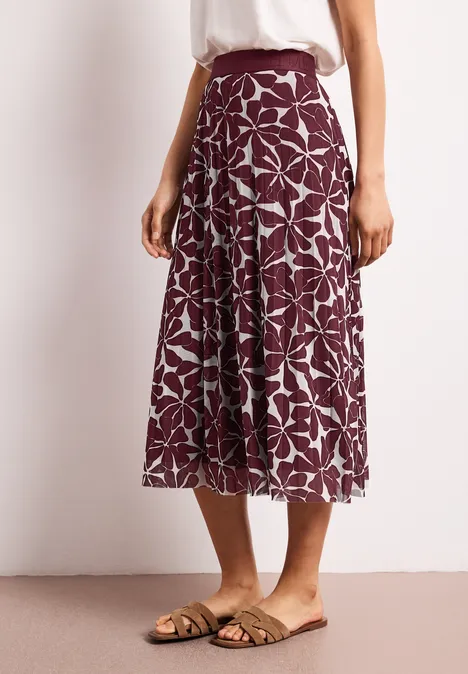 Een persoon draagt een midirok in paars met wit bloemmotief en platte sandalen.