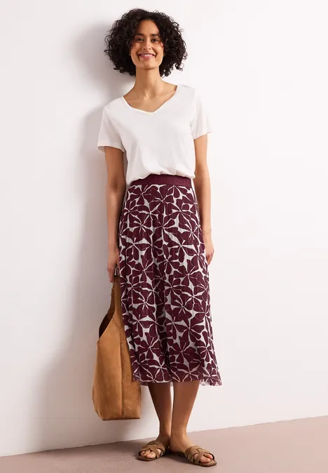 Persoon in wit T-shirt en bordeaux midi-rok met print, met tas.