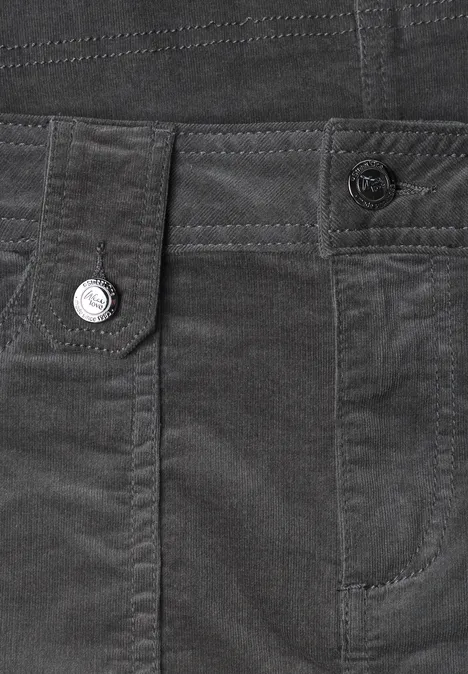 Close-up van een donkergrijze corduroy broek met zakken, riemlussen en knoopdetail.