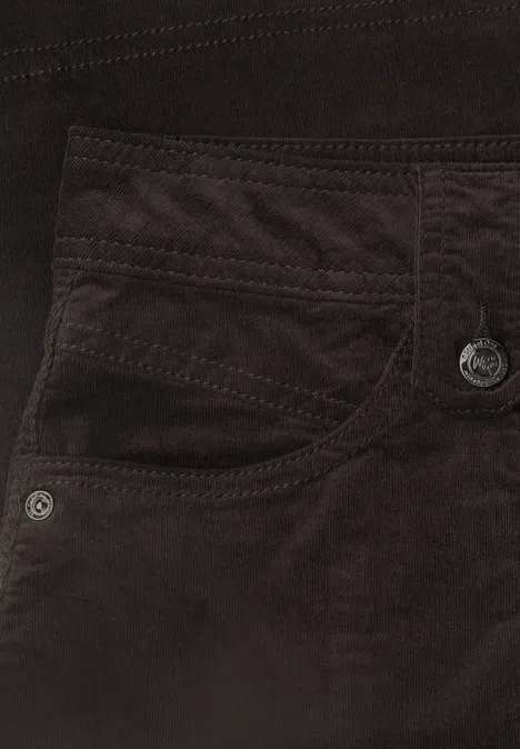 Close-up van een bruine ribfluwelen broek met zakken en sierstiksels.