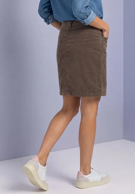 Zijaanzicht van persoon in bruine rok, blauwe blouse en witte sneakers.