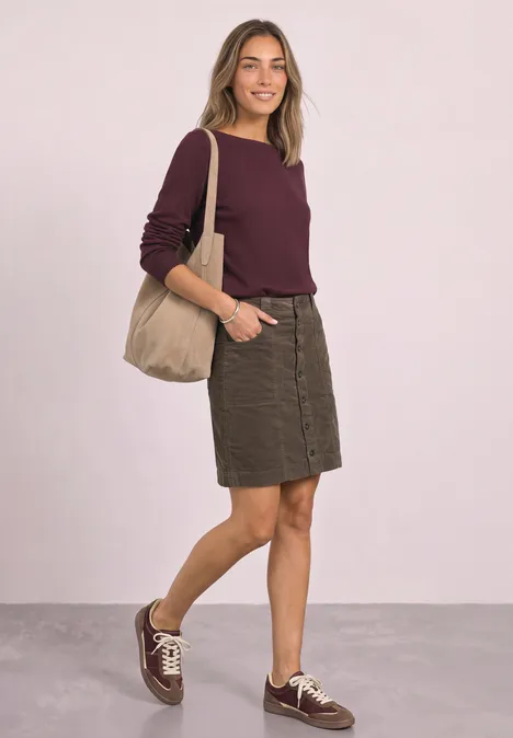 Vrouw in bordeaux trui, kaki rok en laarsjes, met een beige schoudertas.