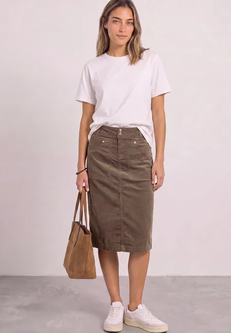 Frau in weißem T-Shirt, braunem Midirock und weißen Sneakern hält eine braune Tasche.