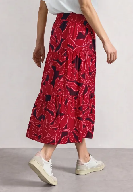 Maxi-Rock mit Volants und Print salsa red Frau trägt einen knöchellangen roten Rock mit abstraktem Blumenmuster und weißen Sneakern.