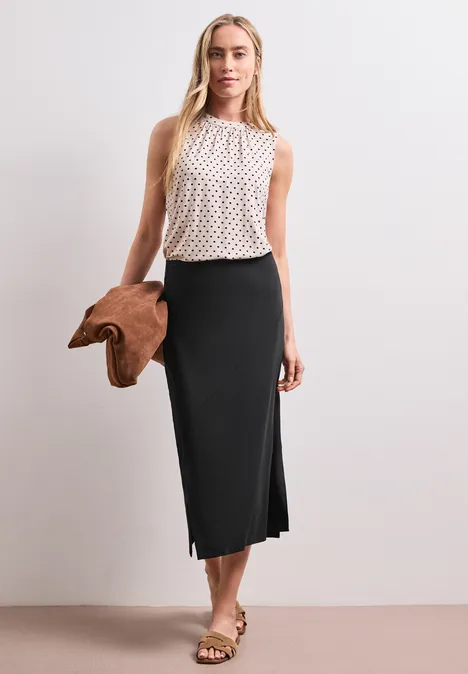 Midirok van tricot in effen kleur Black Vrouw in wit mouwloos topje met stippen en lange zwarte rok, met een bruine tas.