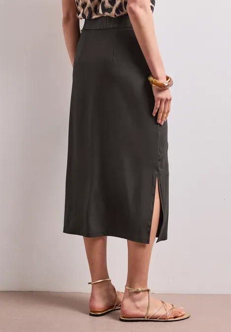 Femme en jupe midi noire fendue sur le côté, top à motif animal et sandales plates.
