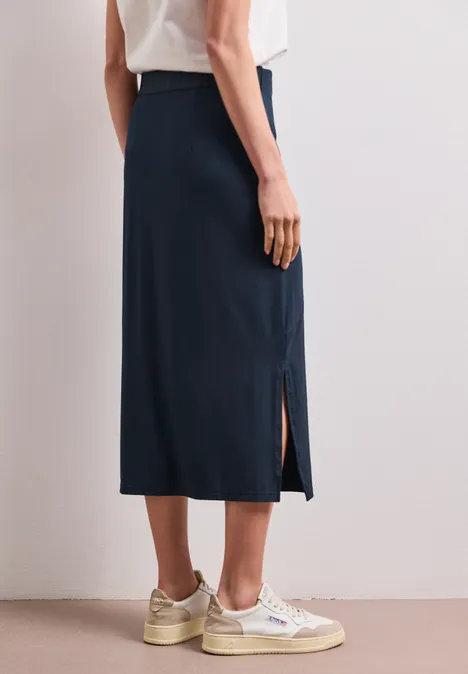 Midirok van tricot in effen kleur shadowed navy Een persoon draagt een lange, donkerblauwe rok met zijsplit en witte sneakers.