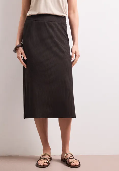 Geribde midirok met elastische tailleband espresso brown Eenvoudige outfit: persoon met een donkere midirok en platte sandalen tegen een neutrale achtergrond.