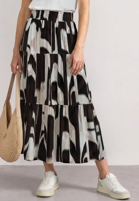 Vrouw in witte top en lange zwart-witte rok met print, witte sneakers en strozak.