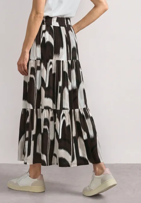 Zwart-witte gelaagde maxi-rok met abstract patroon, gecombineerd met witte sneakers.