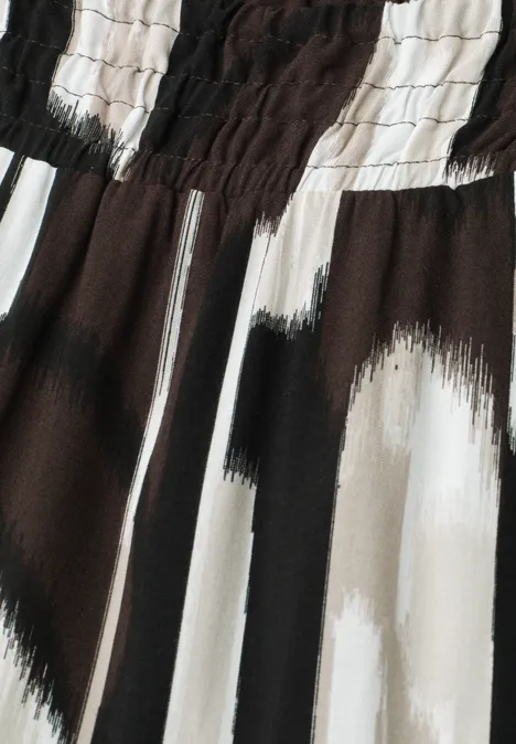Close-up van een stof met elastische taille en abstract penseelstrepenpatroon in zwart, wit en beige.