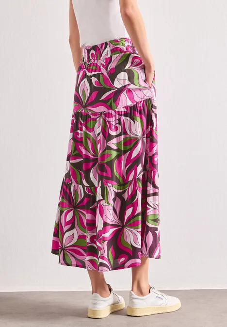 Maxi-Rock mit Volants und Print magenta dream Frau von hinten trägt einen bunten, floralen Maxirock in Pink, Weiß und Grün mit weißen Sneakers.